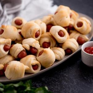 Mini Wurstel in Pasta Sfoglia 8 Piccola ciotola di ketchup accanto a un piatto di mini wurstel in sfoglia dorati appena sfornati pronti da gustare.