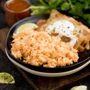 Riso Spagnolo Fatto in Casa 8 riso spagnolo su un piatto con enchiladas guarnite con coriandolo tritato su un tagliere di legno