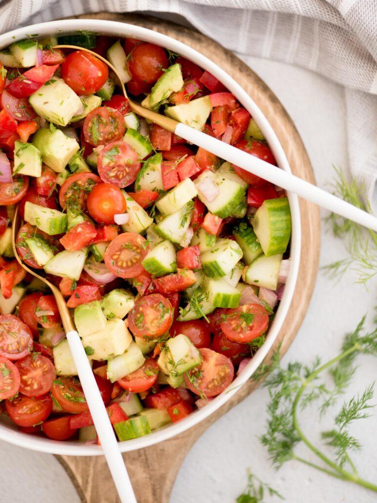 Insalata di Cetrioli, Pomodori, Cipolle e Avocado 8 Vista dall'alto di una grande ciotola di insalata di cetrioli e pomodori con pinze da insalata appoggiate all'interno.