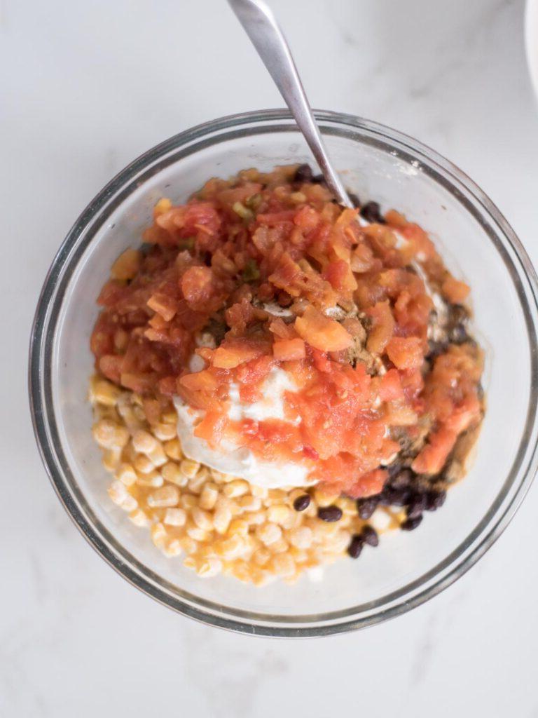 Sformato di Pollo Tex-Mex, Fagioli Neri e Riso 9 Pomodori in scatola (Rotel) aggiunti sopra la miscela di mais e panna acida in una ciotola, per un tocco di acidità e sapore.