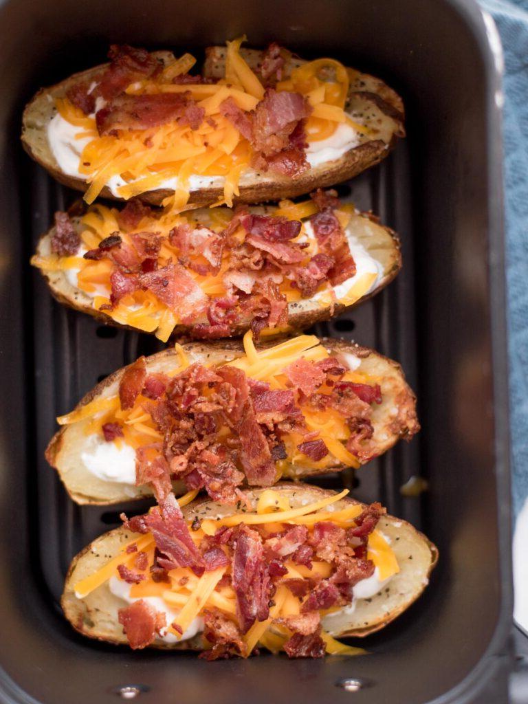 Facili Bucce di Patate in Friggitrice ad Aria 9 4 metà di patate all'interno di un cestello della friggitrice ad aria riempite con panna acida, formaggio e pancetta.