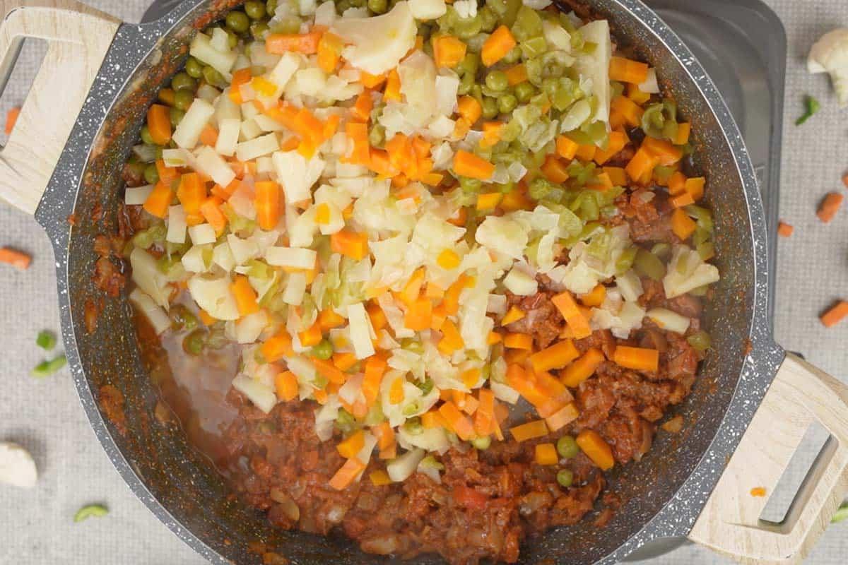 Verdure cotte aggiunte alla padella con la base aromatica, pronte per essere schiacciate.