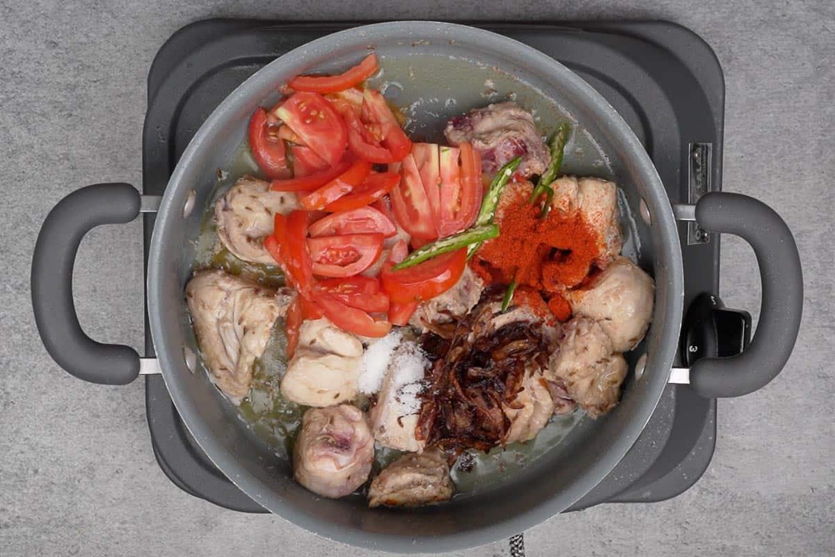 Peperoncini verdi, pomodori, cipolle fritte, sale e peperoncino rosso aggiunti alla pentola.