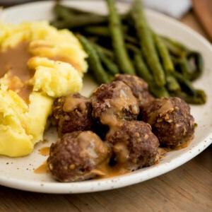 polpette di cipolla alla francese condite con salsa servite su un piatto con purè di patate e fagiolini arrostiti