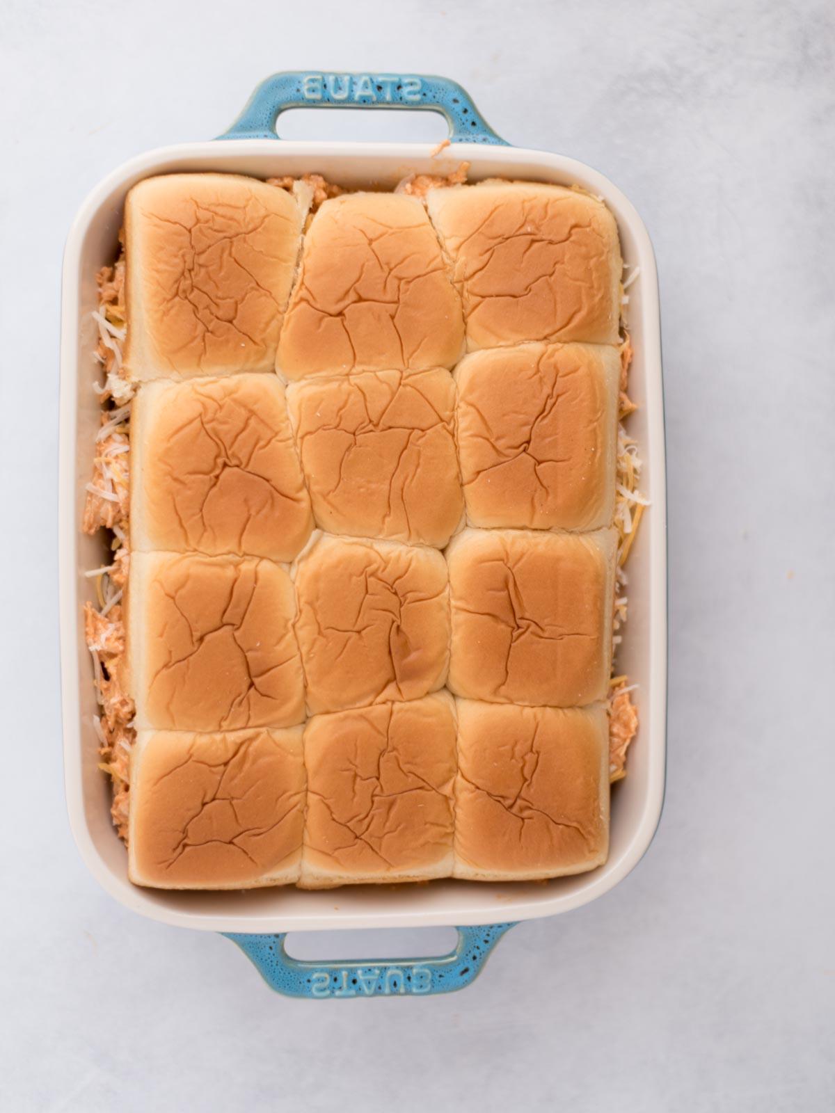 Mini-panini Hawaiani al Pollo Buffalo 10 Panini per sliders coperti con carne condita e formaggio sfilacciato in una teglia.