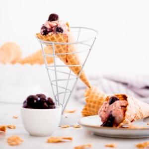 Gelato alle Ciliegie Fatto in Casa 10 Gelato artigianale alle ciliegie nere in un cono con succo di ciliegia che cola lungo il lato - una ciotola piena di ciliegie a lato
