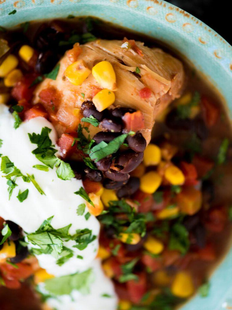 Pollo Messicano a Cottura Lenta 10 Una ciotola di pollo messicano in slow cooker guarnito con coriandolo fresco e panna acida, pronto per essere gustato.