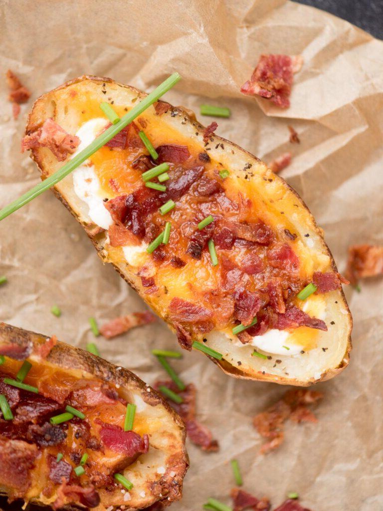 Facili Bucce di Patate in Friggitrice ad Aria 10 Due bucce di patate cotte in friggitrice ad aria riempite con formaggio, pancetta ed erba cipollina su carta forno.