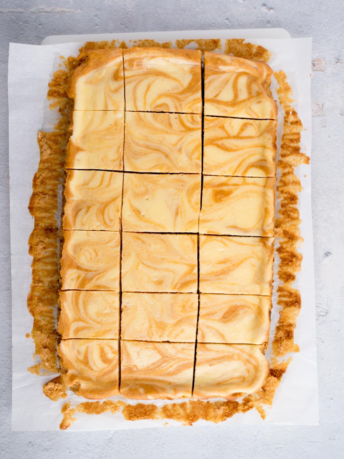Come preparare i Quadrotti di Cheesecake alla Zucca 10 Barrette di cheesecake alla zucca tagliate su carta da forno