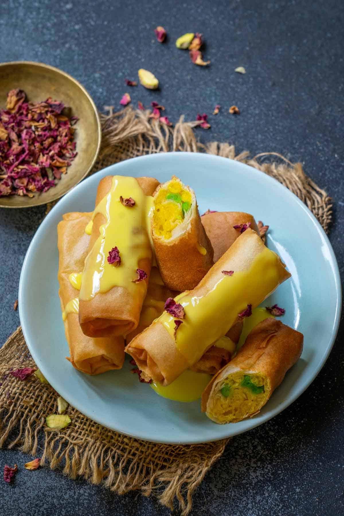 Rotolini di Motichoor 2 Rotoli di Motichoor serviti su un piatto con rabdi e gelato alla vaniglia, un delizioso dessert fusion indiano croccante.