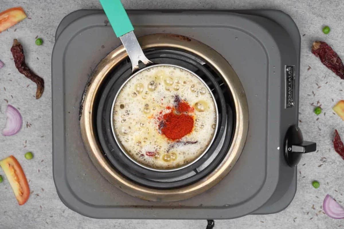 Maggi Tadka Formaggiosa 12 Polvere di peperoncino aggiunta alla padella calda, pronta per essere mescolata.