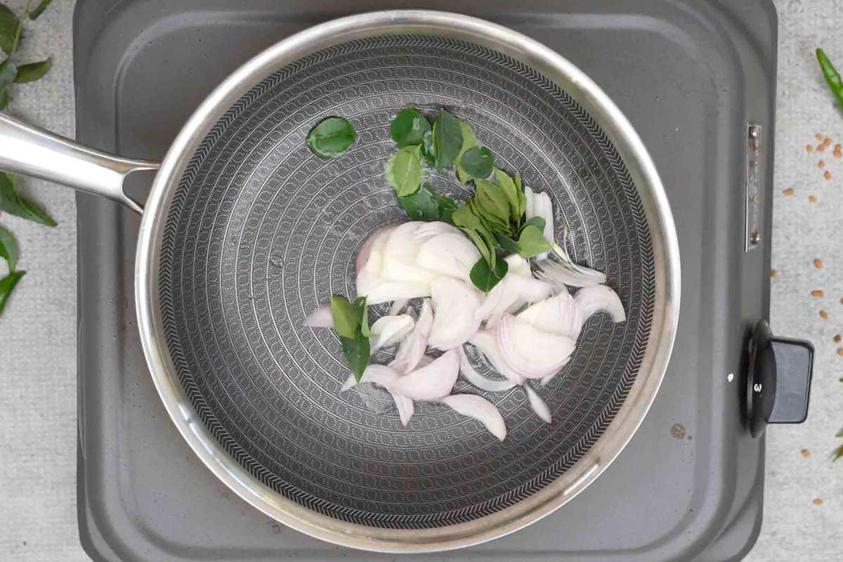 Cipolle e foglie di curry aggiunte alla padella piccola.