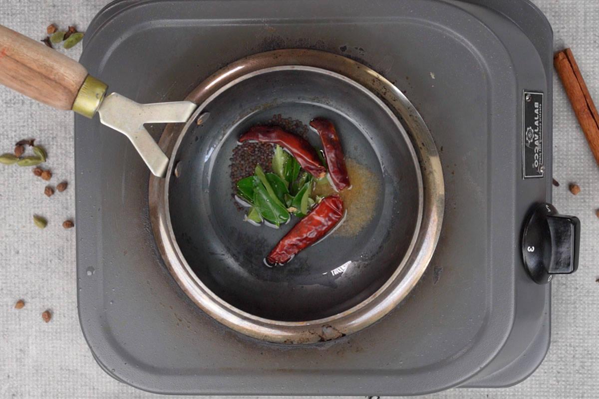 Curry di ceci 17 Semi di senape, assafetida, foglie di curry e peperoncini secchi aggiunti all'olio di cocco caldo in una piccola padella per il tempering.