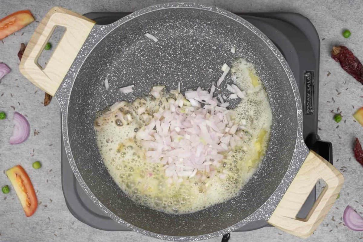 Maggi Tadka Formaggiosa 4 Cipolle tritate aggiunte alla padella con burro caldo, pronte per essere soffritte.