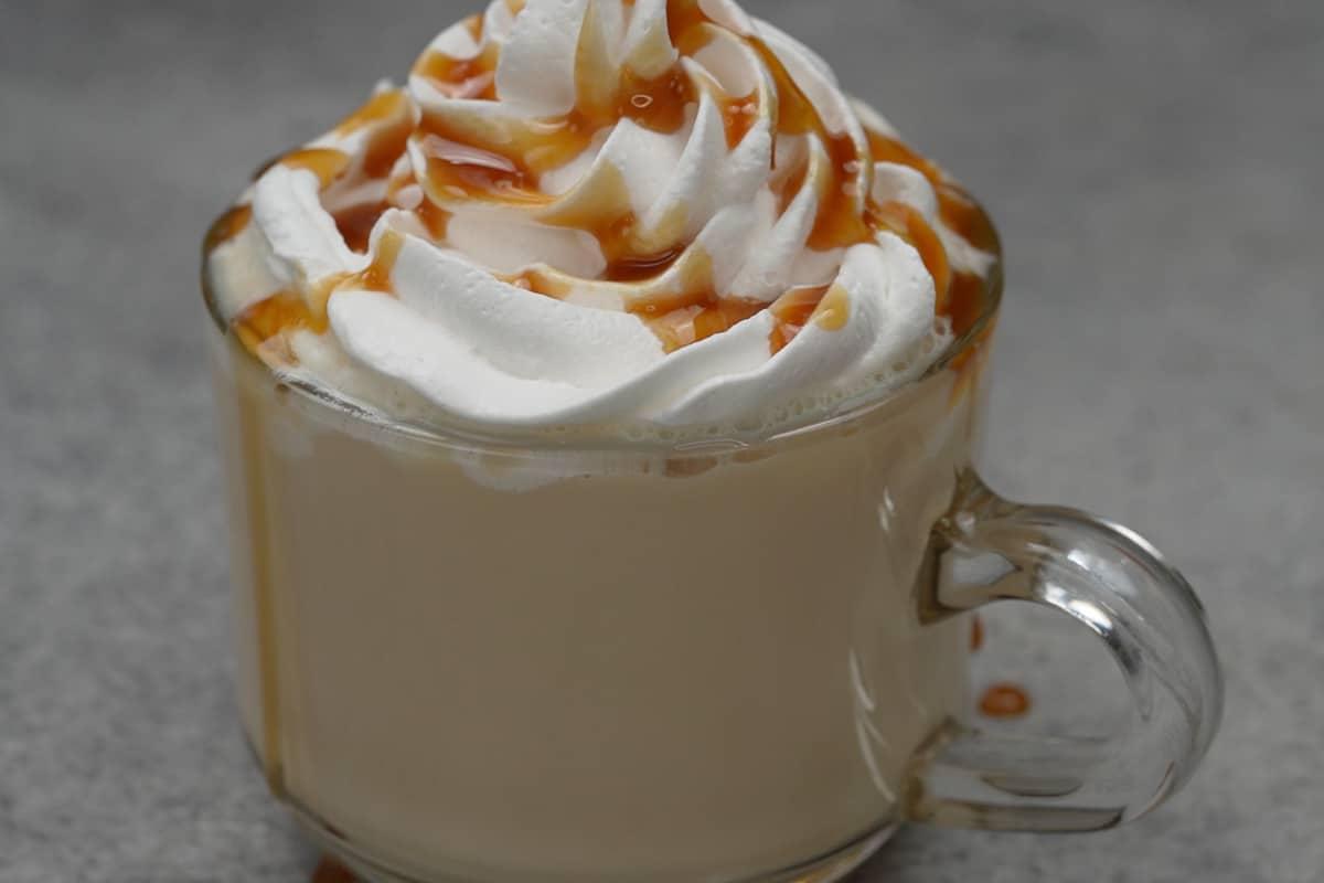 Latte macchiato al caramello pronto, guarnito con panna montata e sciroppo di caramello.