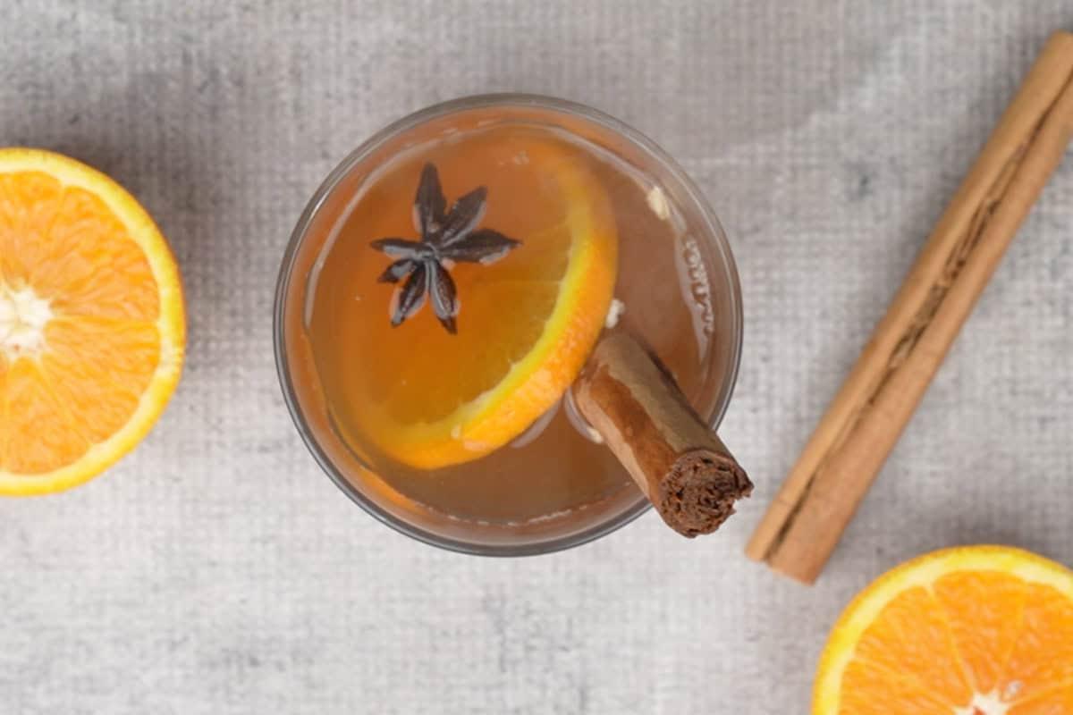 Rum speziato servito in un bicchiere guarnito con cannella, fette d'arancia e anice stellato.