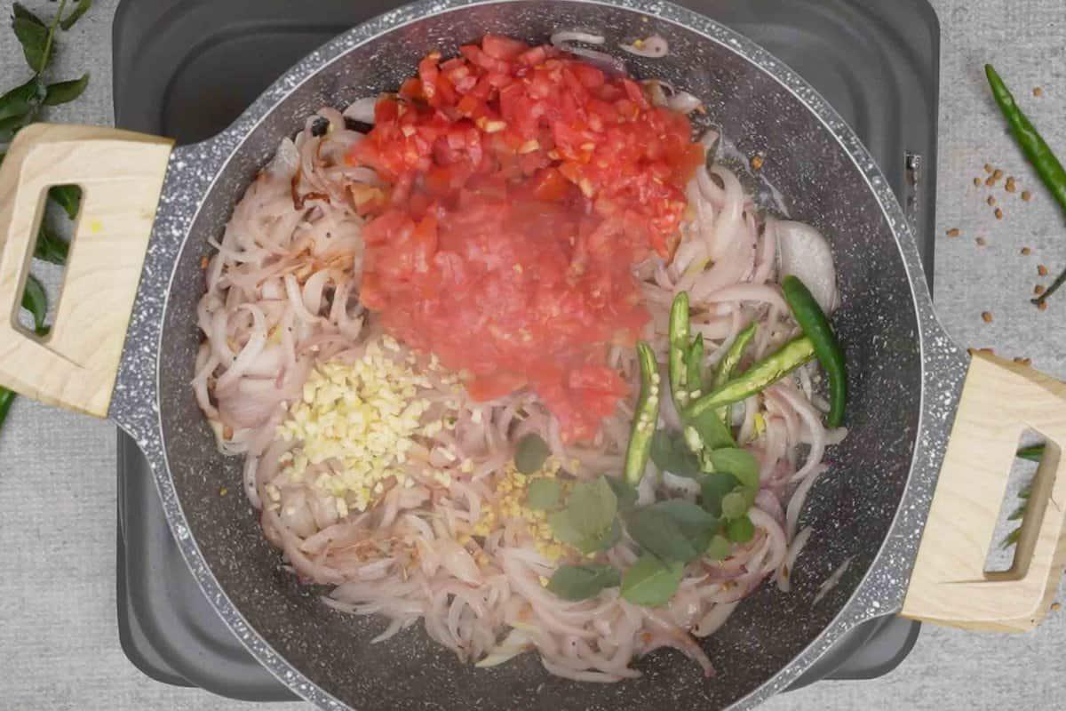 Pomodori, peperoncini verdi, zenzero, aglio e foglie di curry aggiunti alla padella.