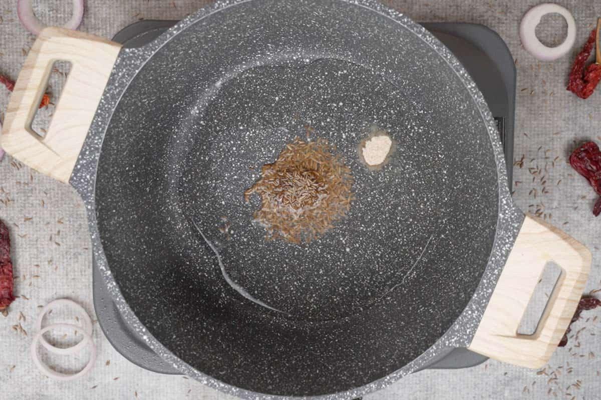 Semi di cumino e asafetida aggiunti alla pentola.