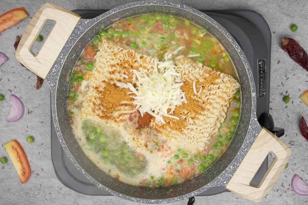 Maggi Tadka Formaggiosa 7 Noodles Maggi, condimento, formaggio grattugiato e garam masala aggiunti alla padella.