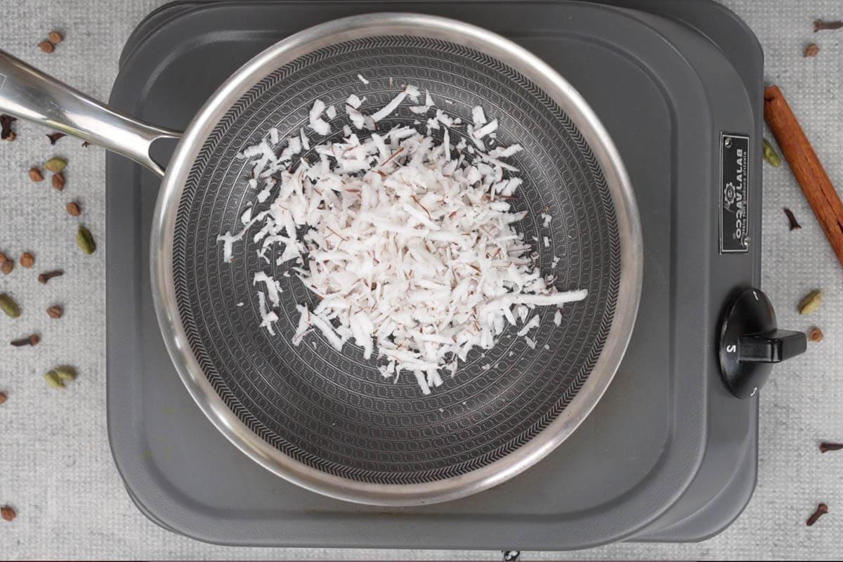 Curry di ceci 6 Cocco fresco grattugiato aggiunto a una padella per essere tostato.
