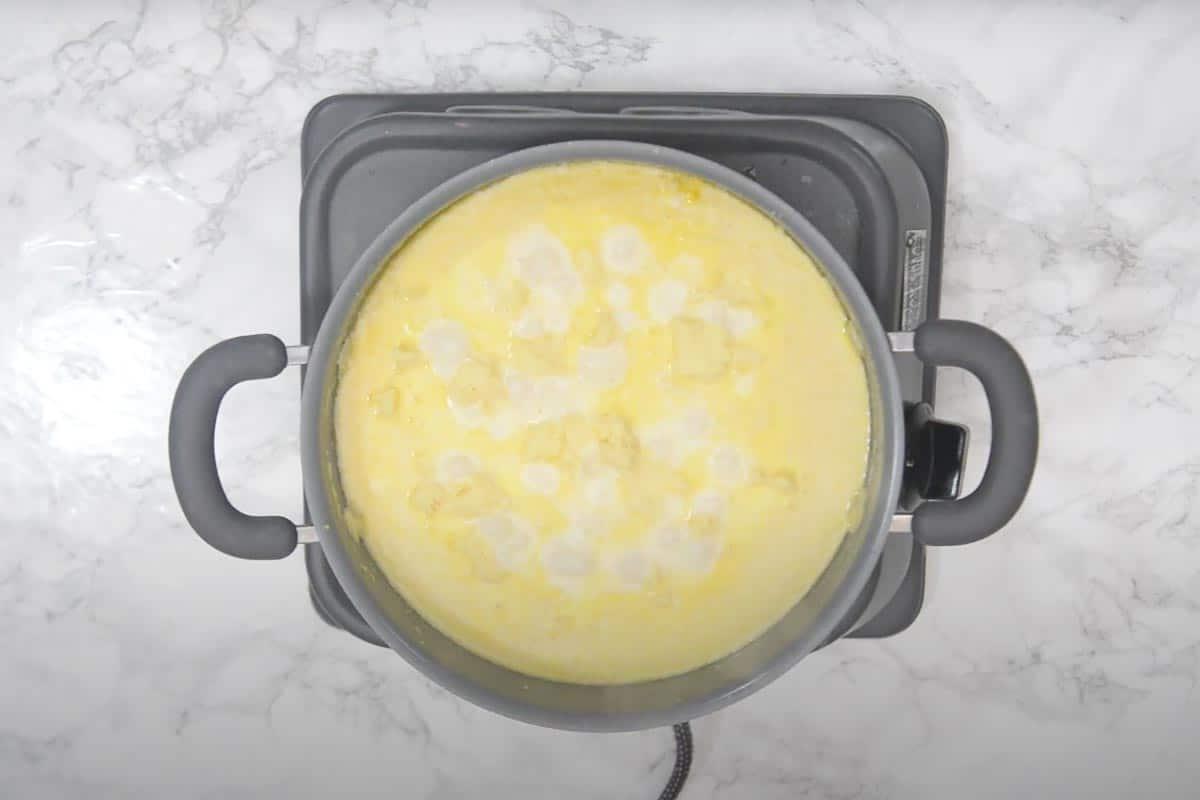 Halwa di Moong Dal 10 Khoya sbriciolato aggiunto nella padella con il composto di Moong Dal e latte, pronto per essere mescolato.