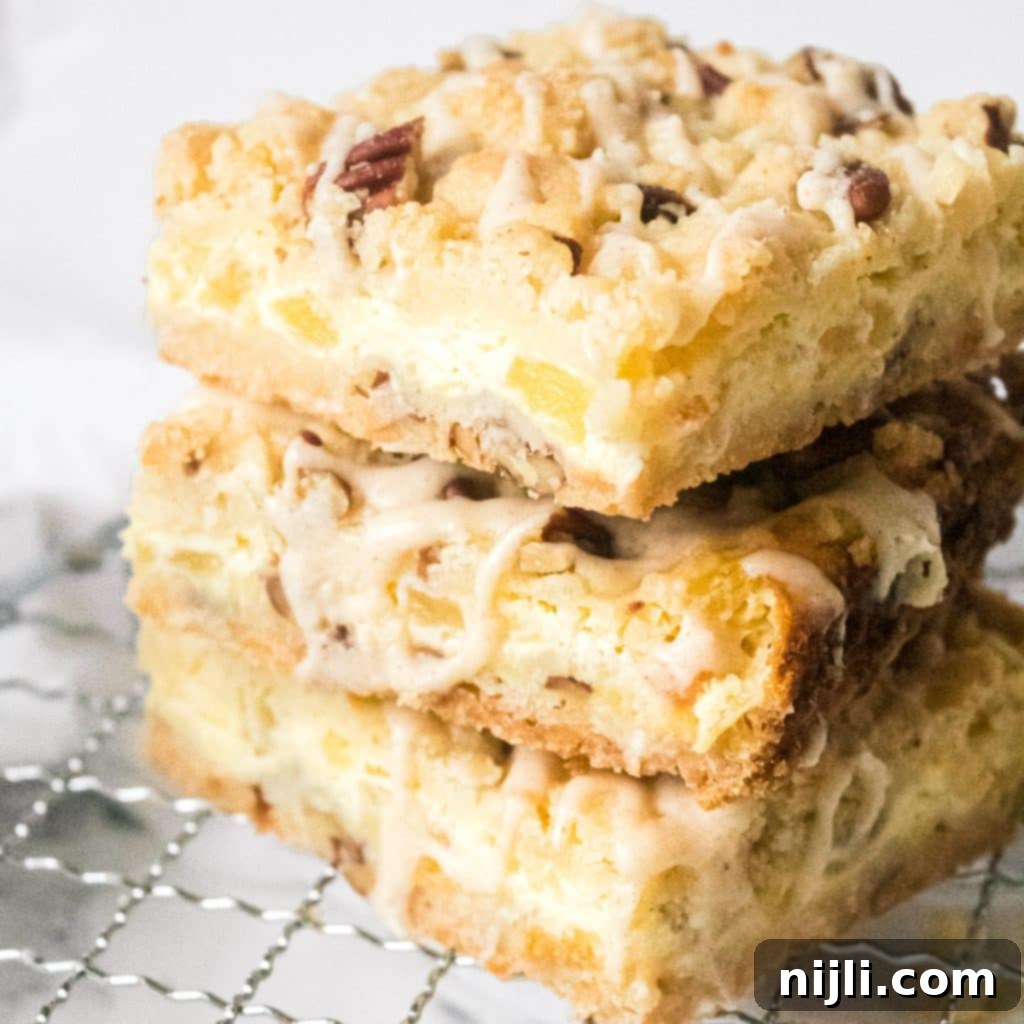 Close up stack of pineapple bars on a wire rack, showcasing the layers of crust, filling, and topping, ready to be enjoyed.