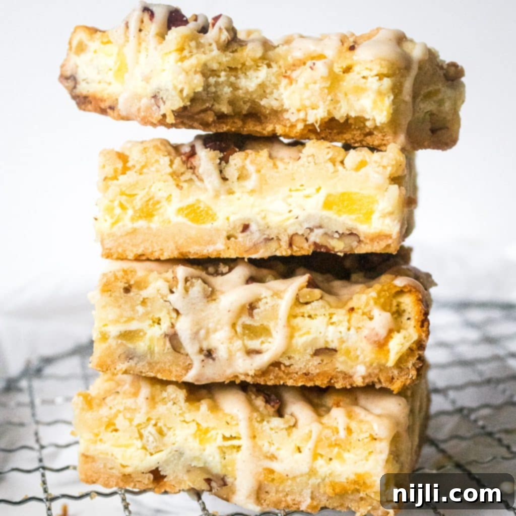 Close up stack of pineapple bars on a wire rack, showing the intricate layers and the glistening coconut drizzle on top.