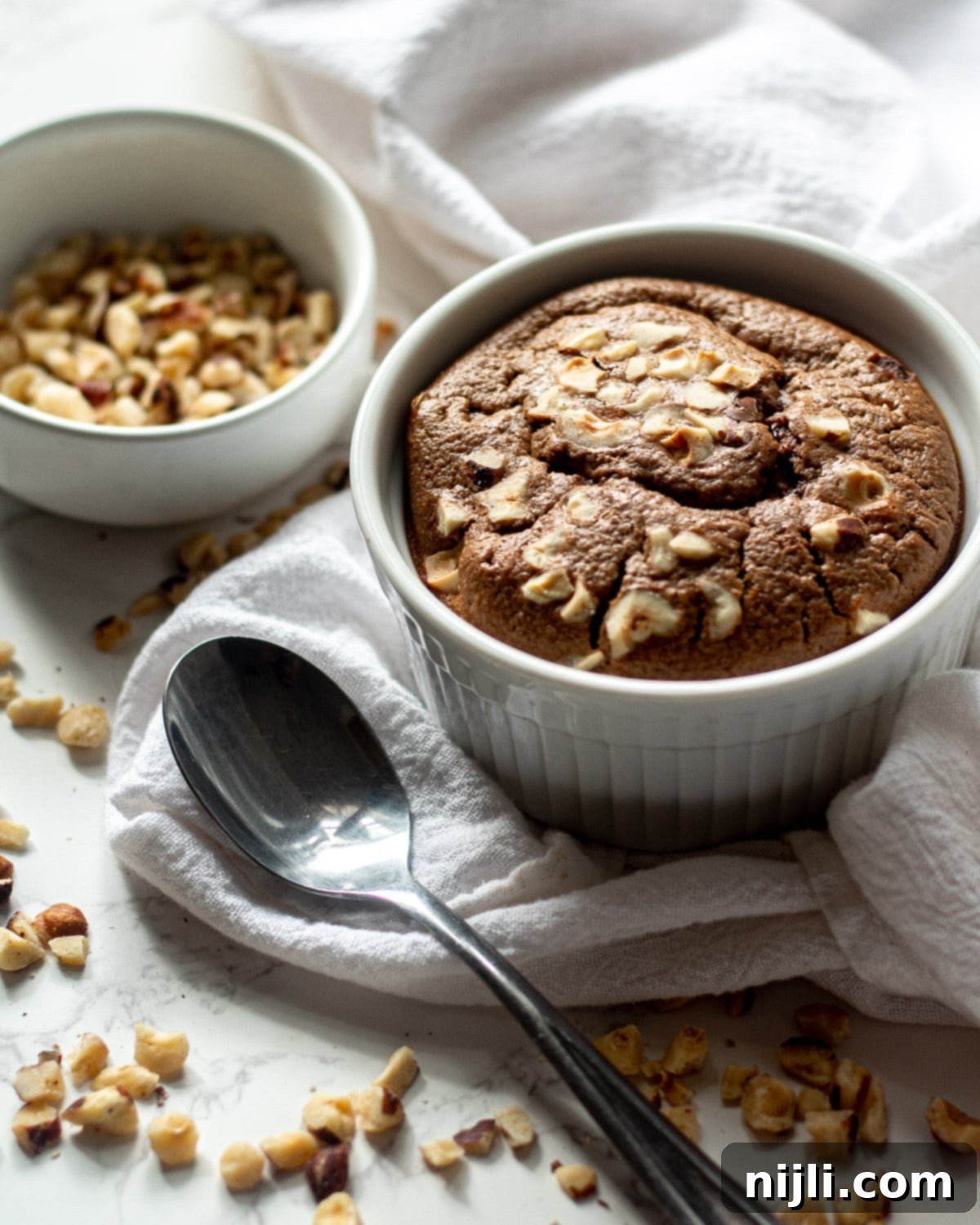 Indulgent Nutella Baked Oats 4 nutella baked oats in the ramekin with hazelnuts in a bowl and scattered around