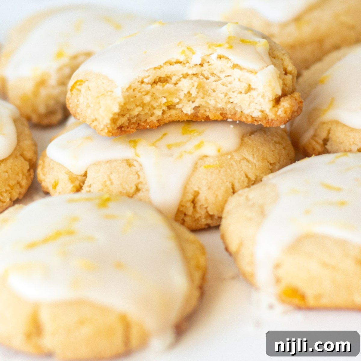 Nutty Lemon Bliss Cookies 2 Iced almond lemon cookies, with one showing a bite taken out, highlighting the soft interior and bright lemon glaze.