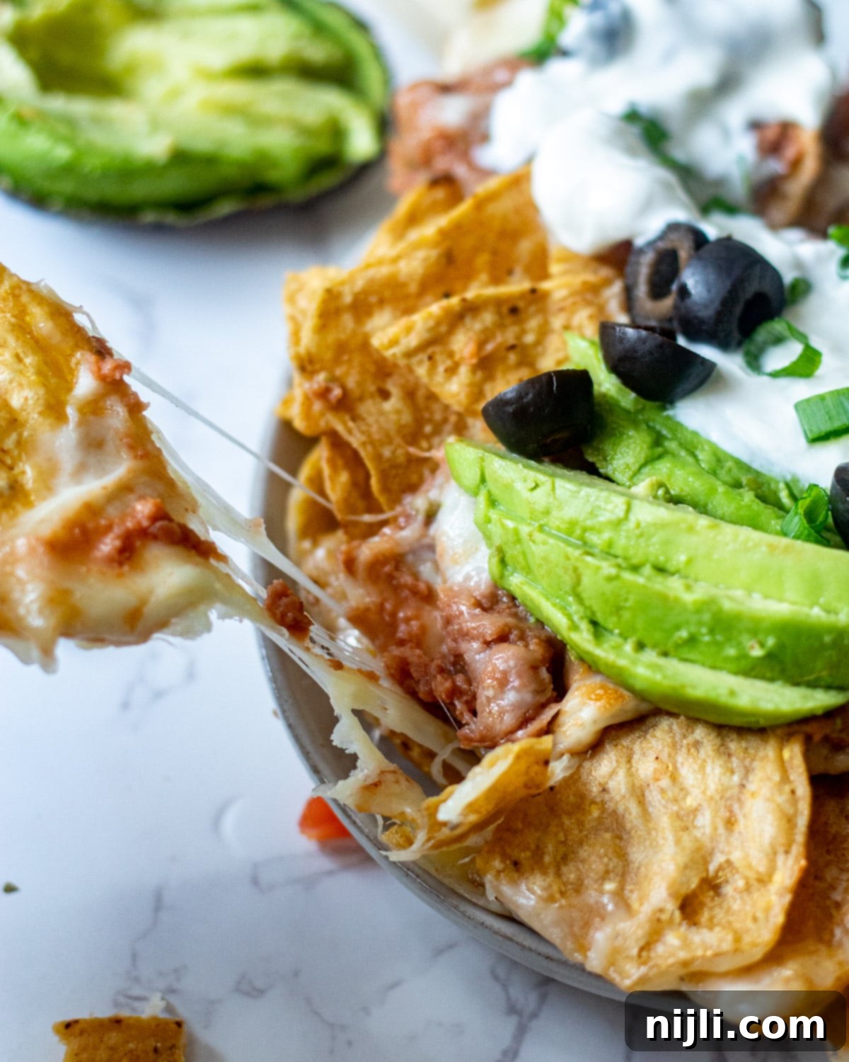 Crispy Air Fryer Nachos 3 Close-up of a hand pulling a chip from freshly made air fryer cheese nachos, highlighting the perfect melt and golden chips