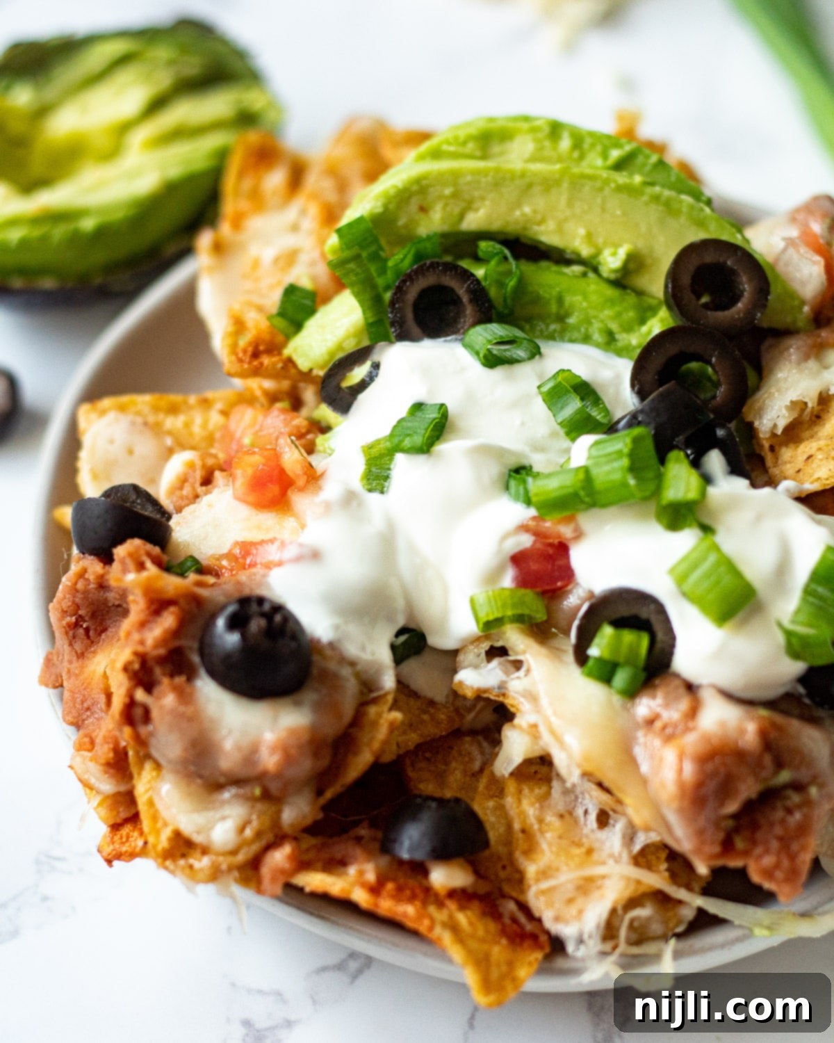 Crispy Air Fryer Nachos 6 A beautifully arranged plate of air fryer nachos with melted cheese, fresh pico de gallo, sliced avocado, and a dollop of sour cream, ready to be enjoyed.