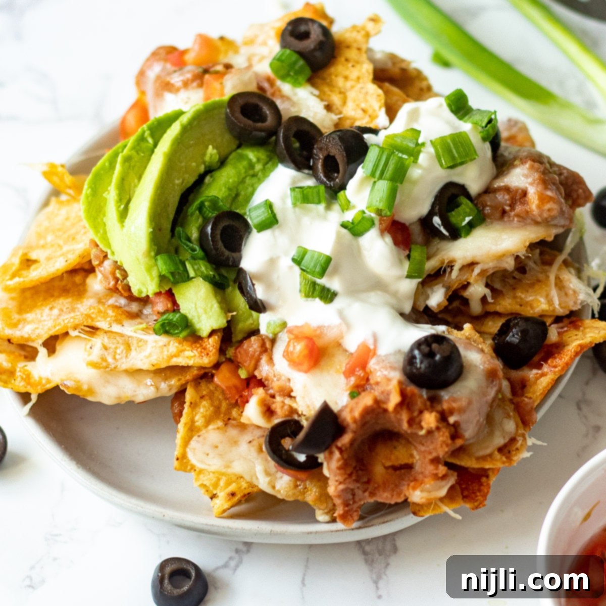 Crispy Air Fryer Nachos 7 Air fryer nachos on a plate with melted cheese, refried beans, and toppings