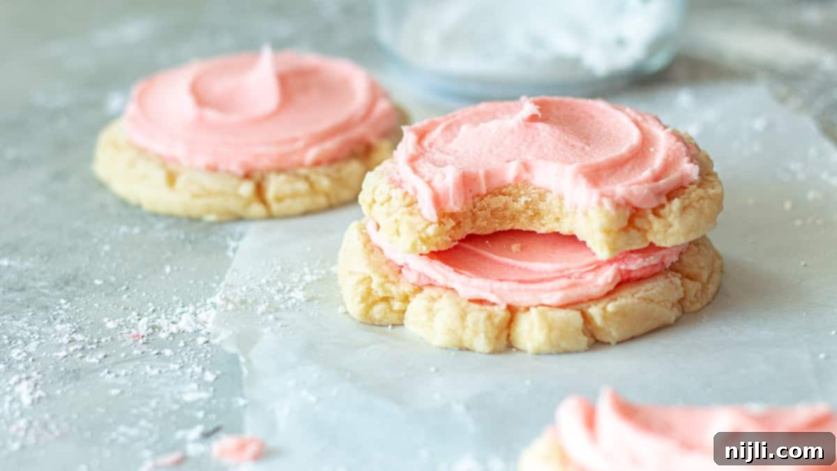 Copycat Crumbl Sugar Cookies 3 a frosted crumbl chilled sugar cookie with a bite taken out stacked on top of another cookie