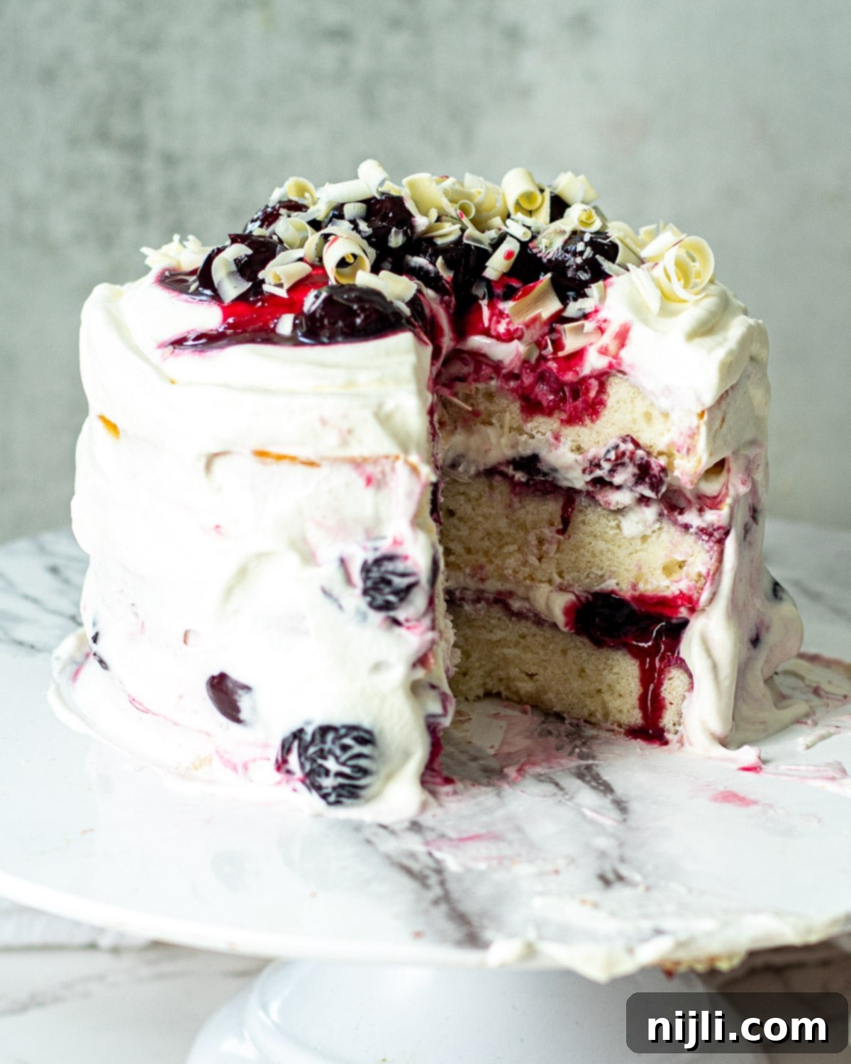 Snow-Kissed Forest Cake 4 A slice of White Forest Cake next to a whole White Forest Cake, showing its beautifully layered interior with cherry filling and whipped cream.