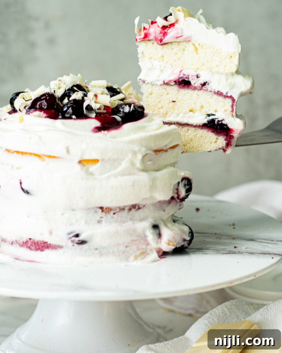 Snow-Kissed Forest Cake 6 A perfectly cut piece of White Forest Cake, showcasing the fluffy white cake, cherry filling, and whipped cream layers.