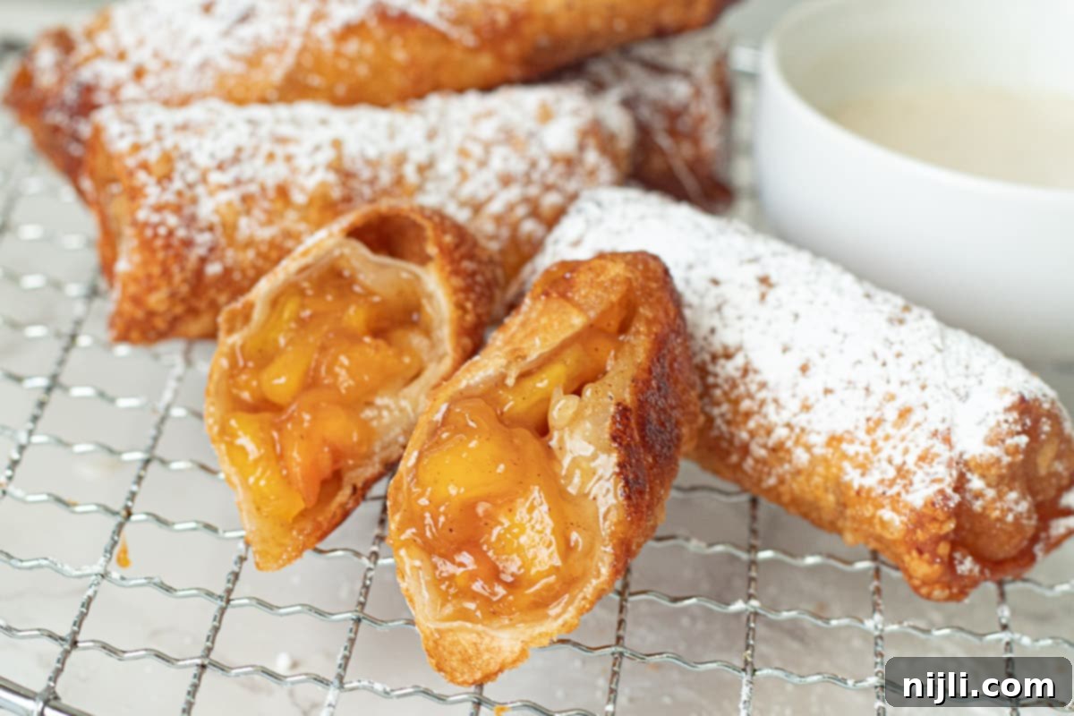Peach Cobbler Egg Rolls 5 peach cobbler egg rolls on a tray with icing