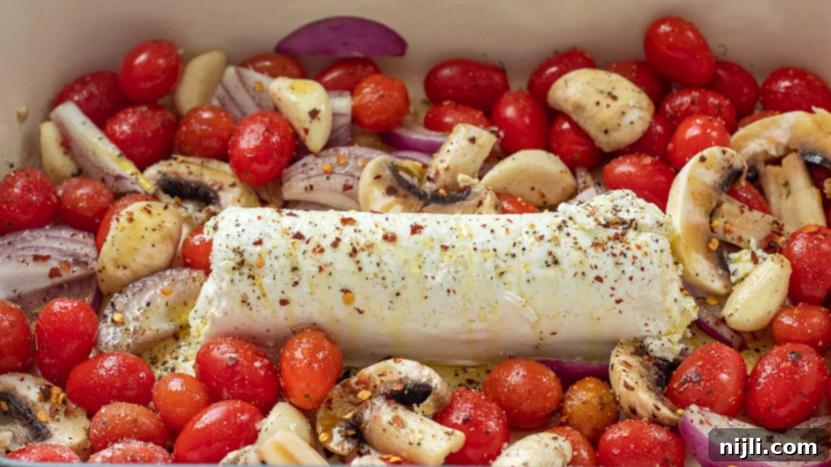 Creamy Goat Cheese Pasta Bake 4 Goat Cheese Tomato Pasta Sauce baking in the oven, with a log of goat cheese surrounded by tomatoes, garlic, and mushrooms