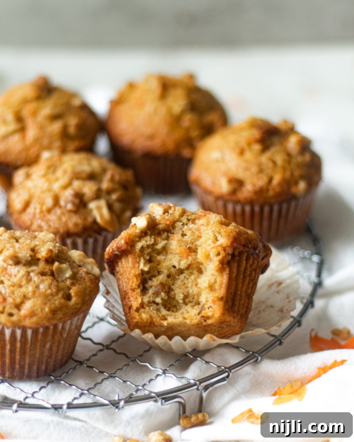 Golden Carrot Banana Muffins 4 Simple banana carrot muffins on a rack, one with a bite taken out, highlighting the moist texture.