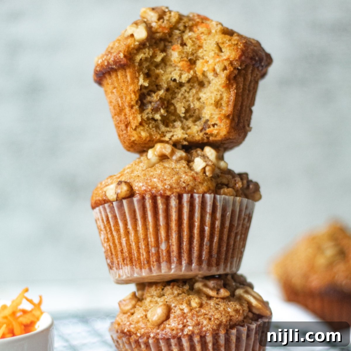 Golden Carrot Banana Muffins 8 Stacked banana carrot muffins, one with a bite taken out