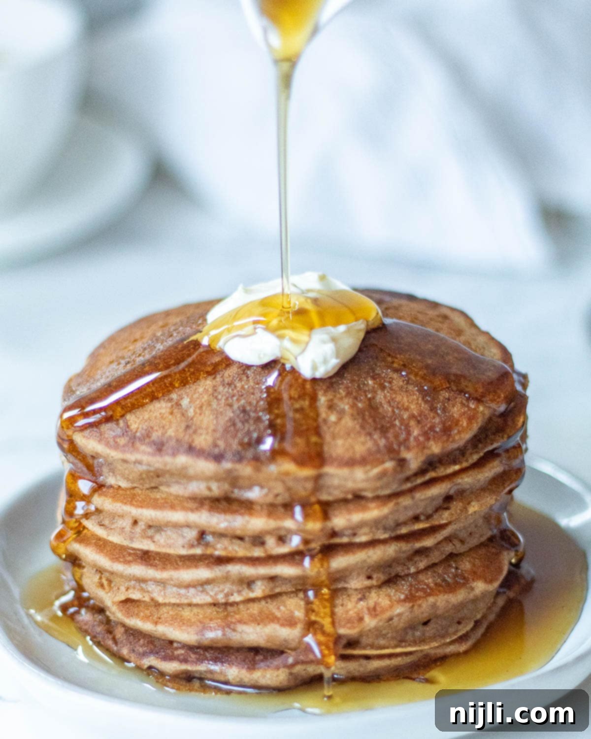 Fluffy Oat Milk Bliss 3 Stacked fluffy oat milk pancakes drizzled generously with butter and maple syrup.