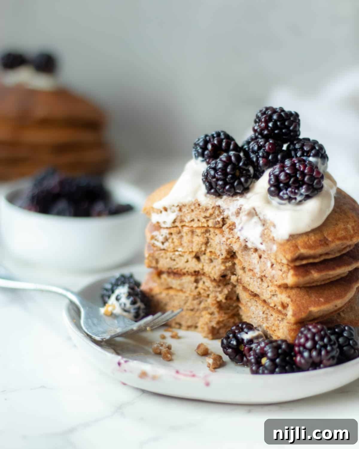 Fluffy Oat Milk Bliss 4 A stack of oat milk pancakes on a plate, with a piece cut out, ready to be enjoyed.