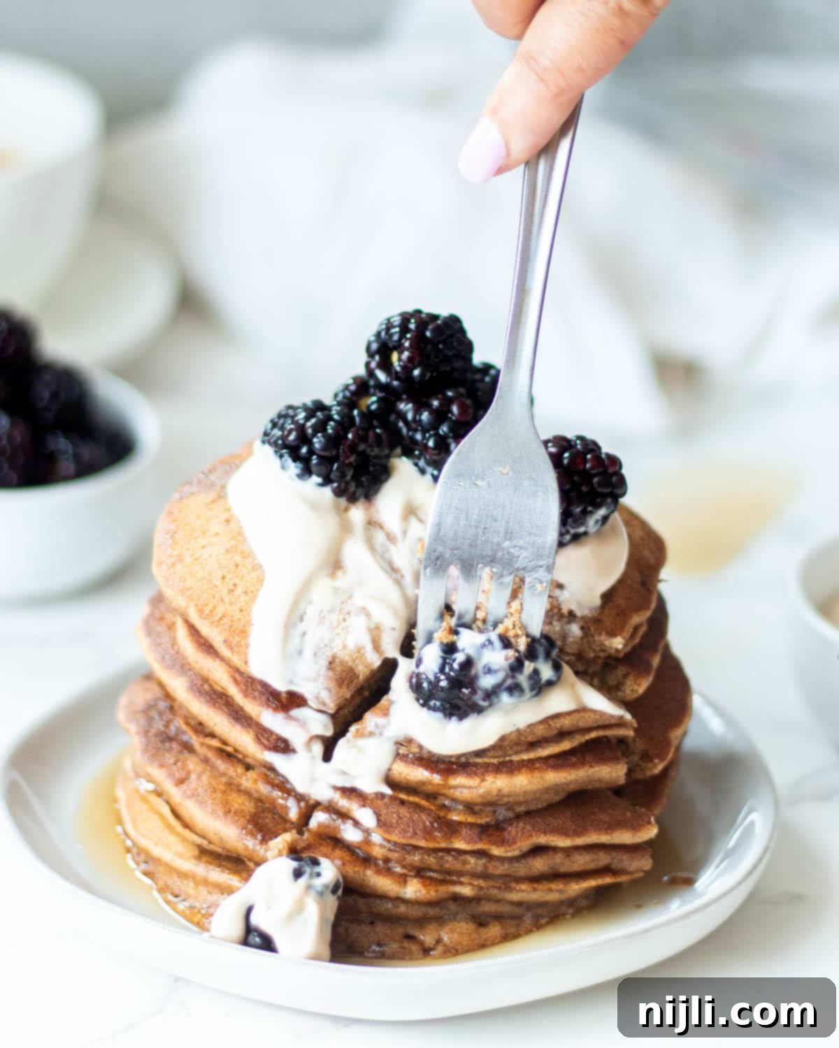 Fluffy Oat Milk Bliss 6 A fork cutting into a stack of fluffy oat milk pancakes, showing the soft interior. This is the no-egg version.