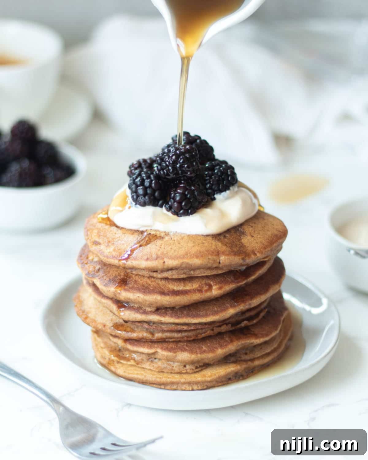Fluffy Oat Milk Bliss 8 A tall stack of oat milk pancakes, garnished with fresh blackberries and a dollop of dairy-free yogurt.