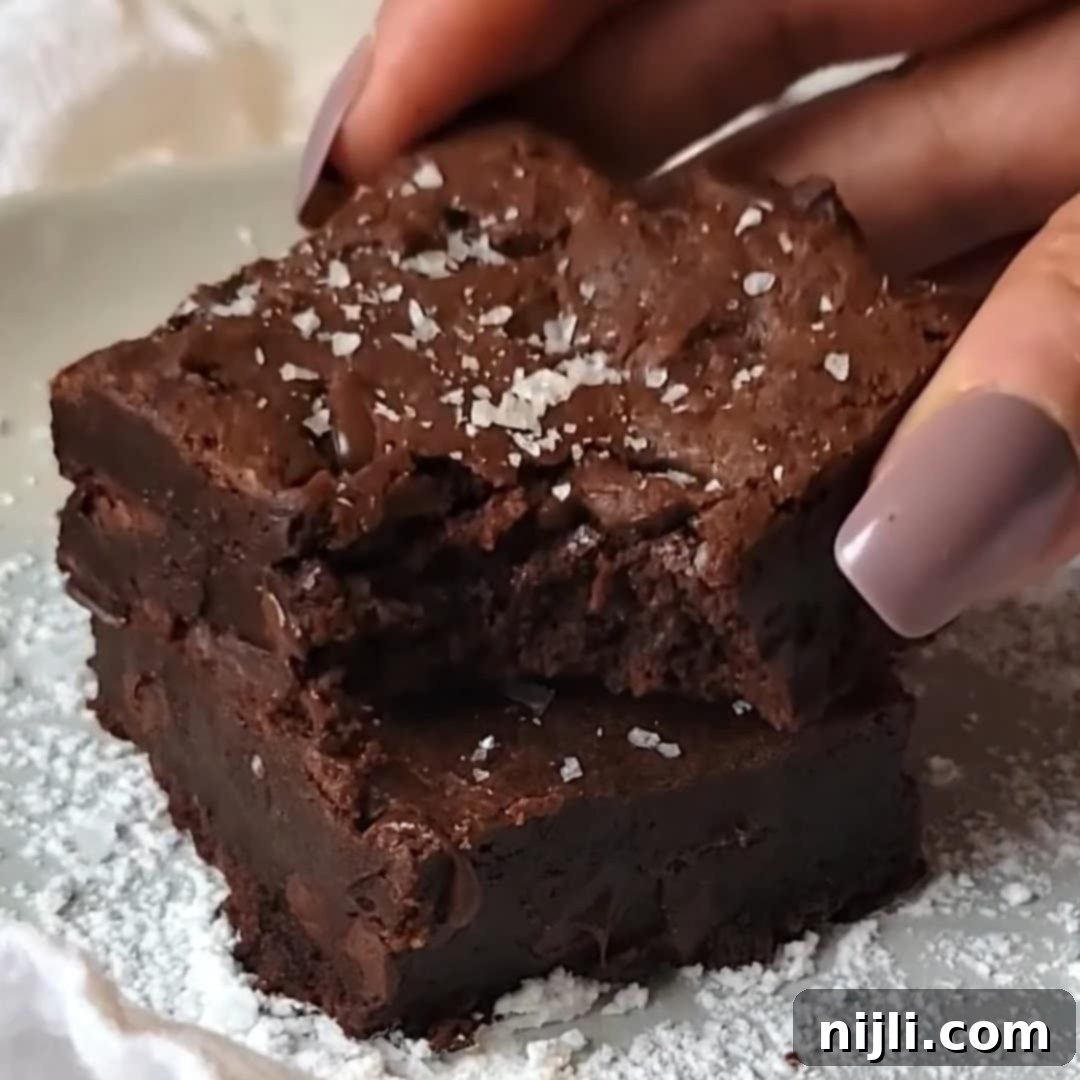 A stack of condensed milk brownies, one with a bite taken out, and a hand picking that one up.