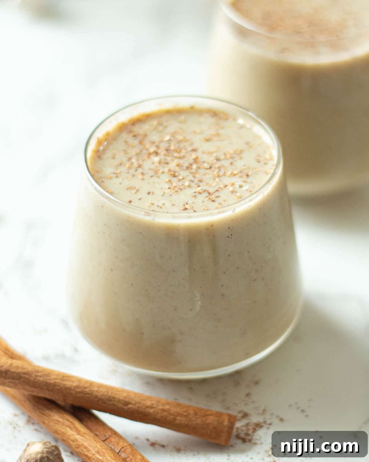 Spiced Oat Milk Cheer 12 A glass of creamy Planet Oat Milk eggnog, topped with a dash of cinnamon, showcasing its smooth texture.
