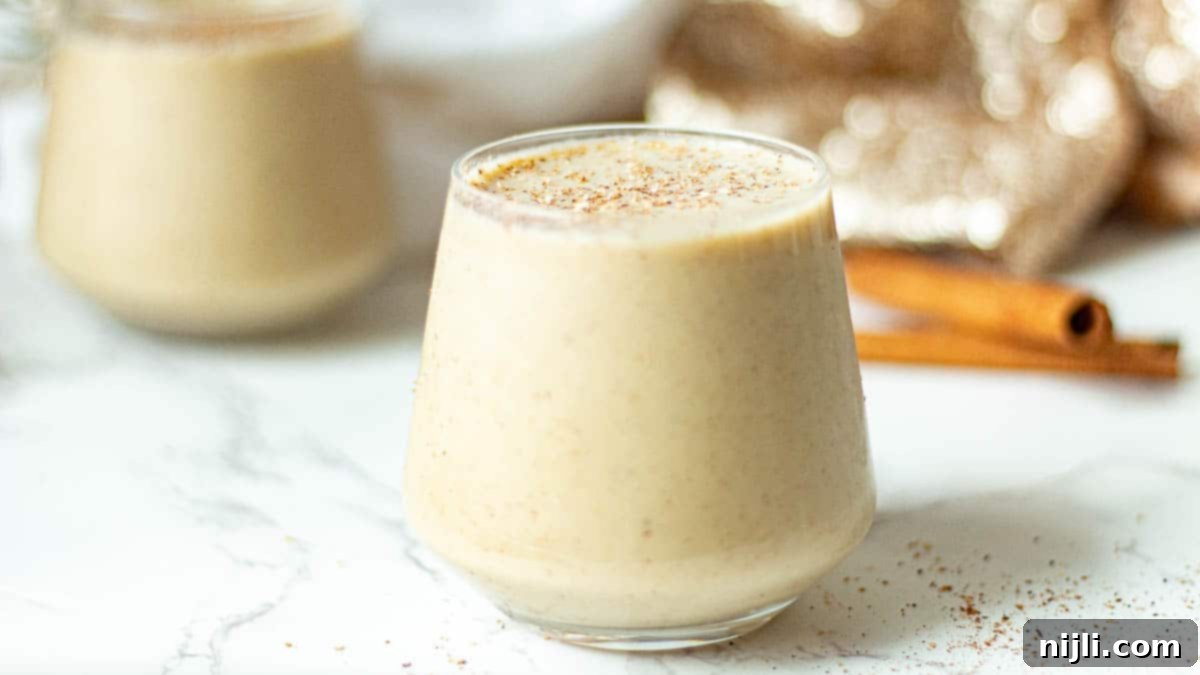 Spiced Oat Milk Cheer 3 Two glasses of vegan oat nog, garnished with a sprinkle of spices, ready for a festive gathering.