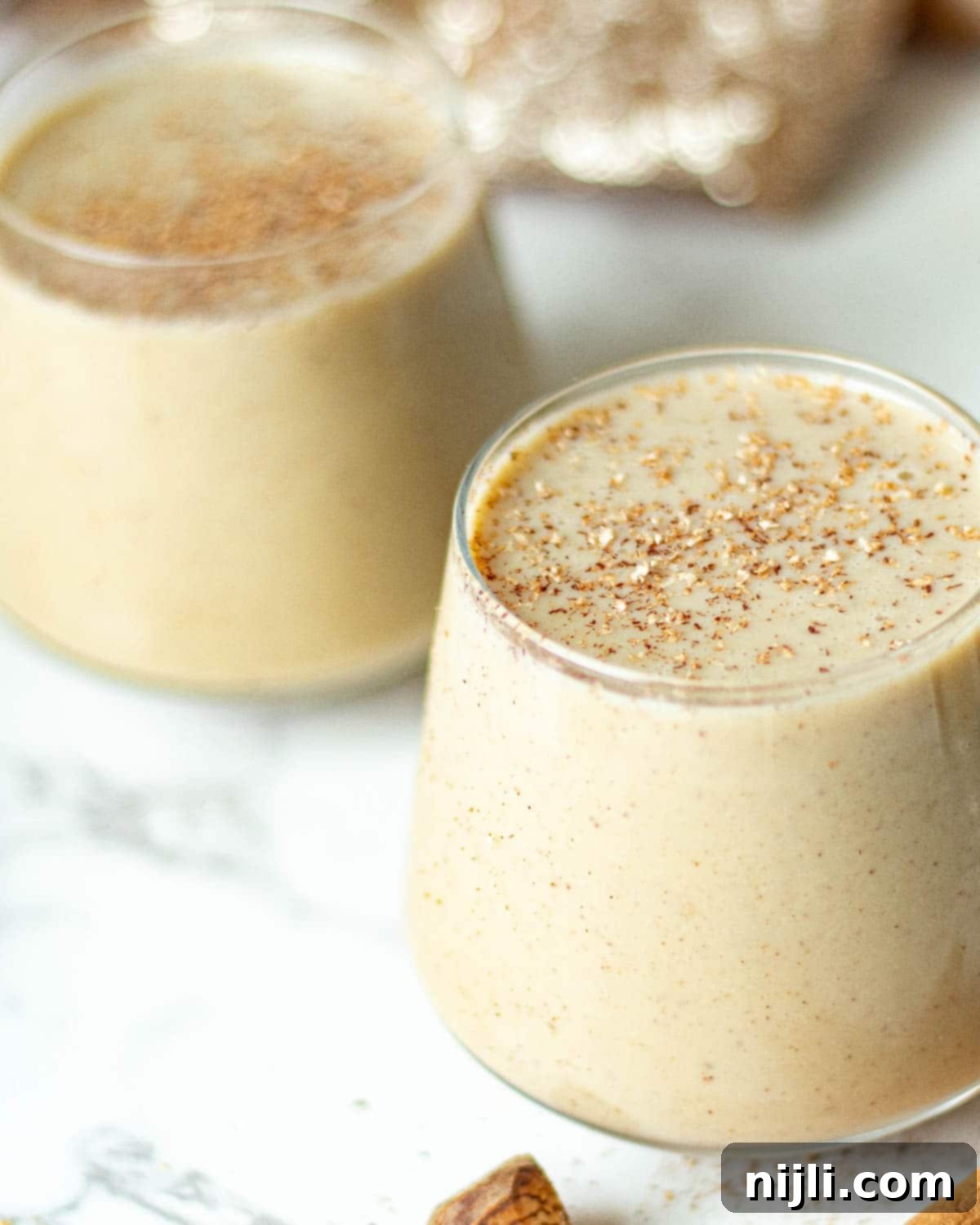 Spiced Oat Milk Cheer 5 Glasses of creamy non-dairy eggnog, garnished with cinnamon sticks and a sprinkle of nutmeg, ready to be served.