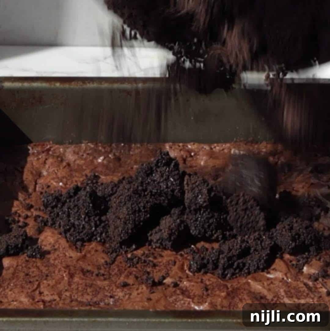 Tombstone Brownies 6 Step 1: Spreading crushed Oreo crumbs on top of baked brownies to create a 'dirt' layer.
