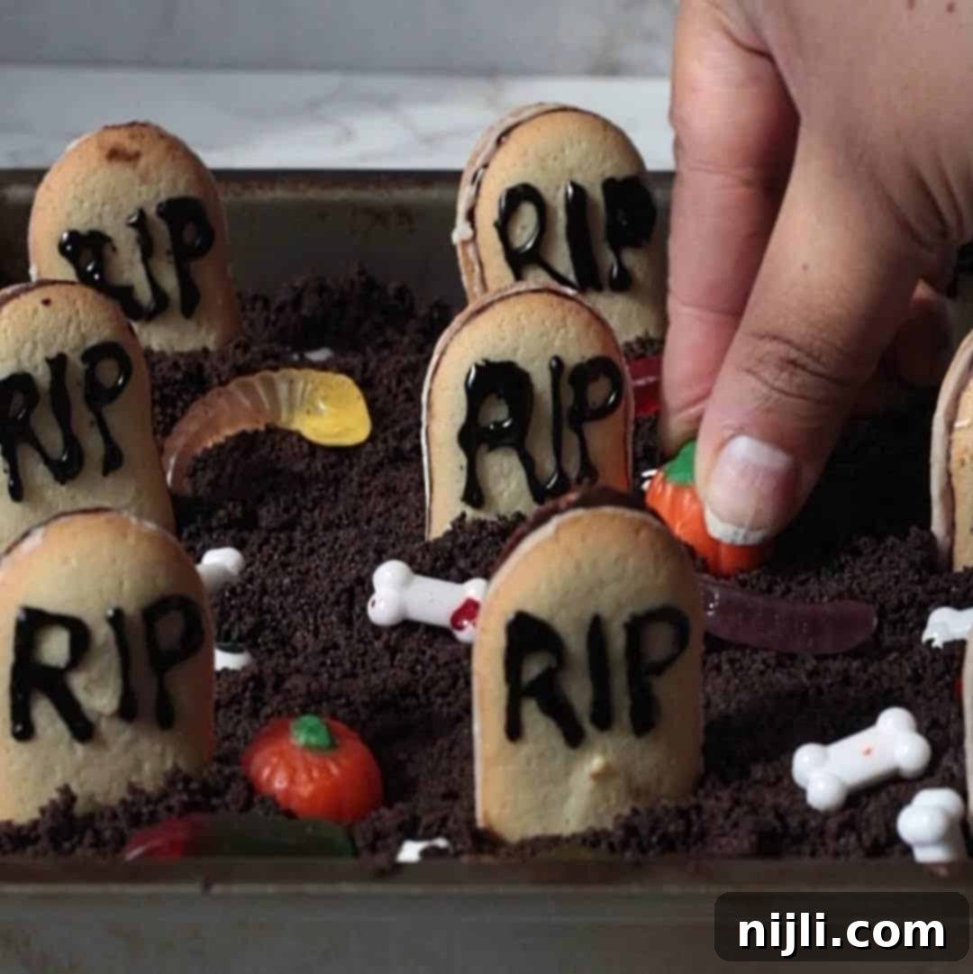 Tombstone Brownies 8 Step 3: Scattering candy pumpkins, bones, eyes, and gummy worms around the tombstones on the graveyard brownies.