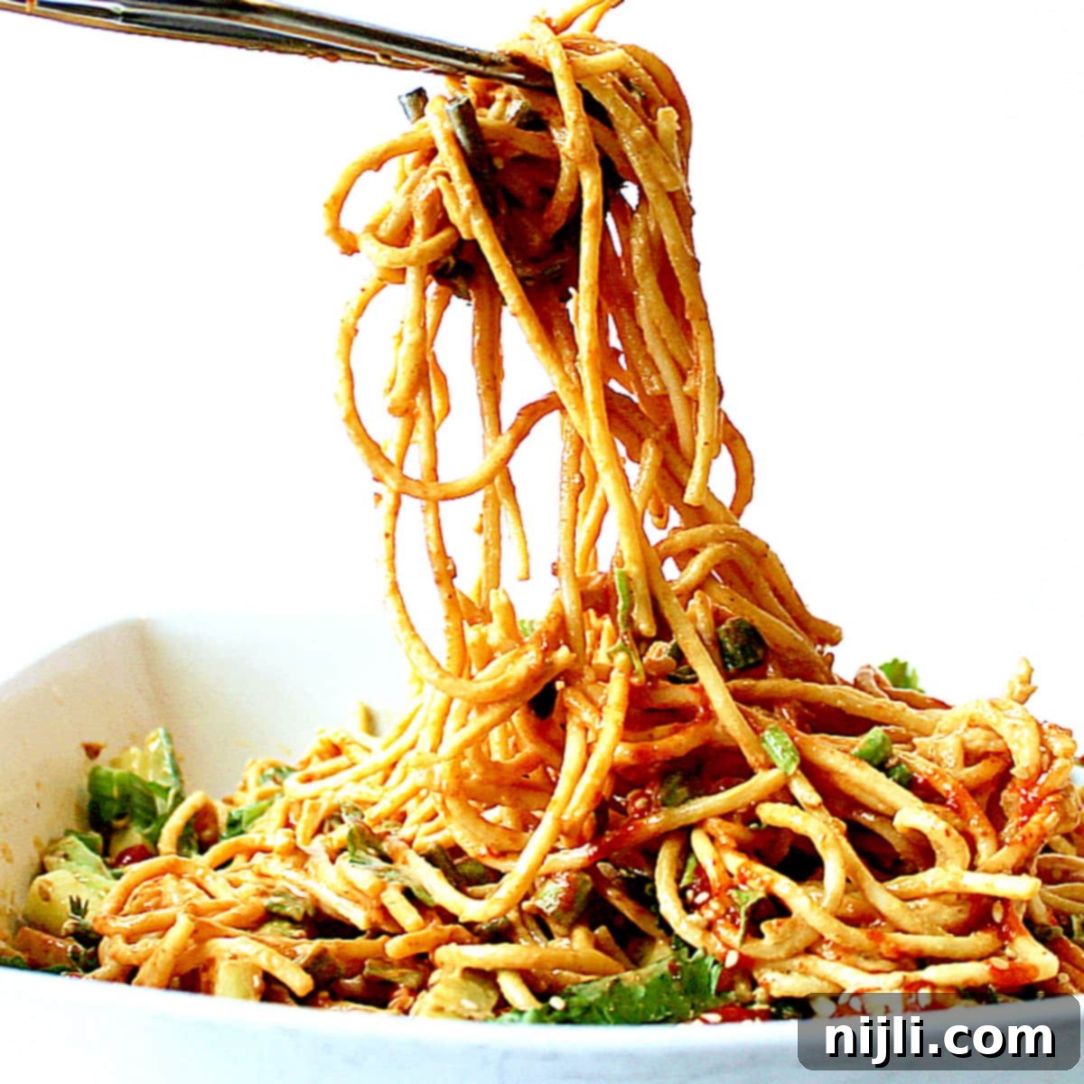Creamy Peanut Noodle Salad 2 tongs serving peanut noodle salad from a bowl